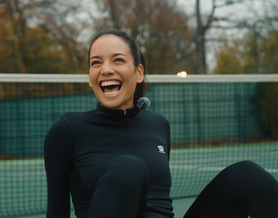 Sportive souriante assise devant un filet de tennis, micro-cravate au col