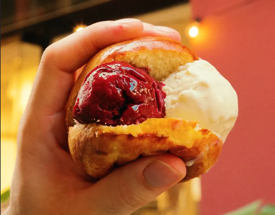 Main tenant une brioche garnie de glace et de coulis de fruits rouges