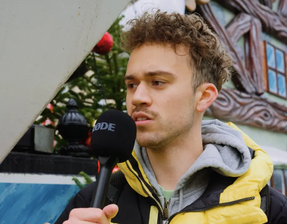 Jeune homme interviewé au micro dans une rue décorée pour Noël