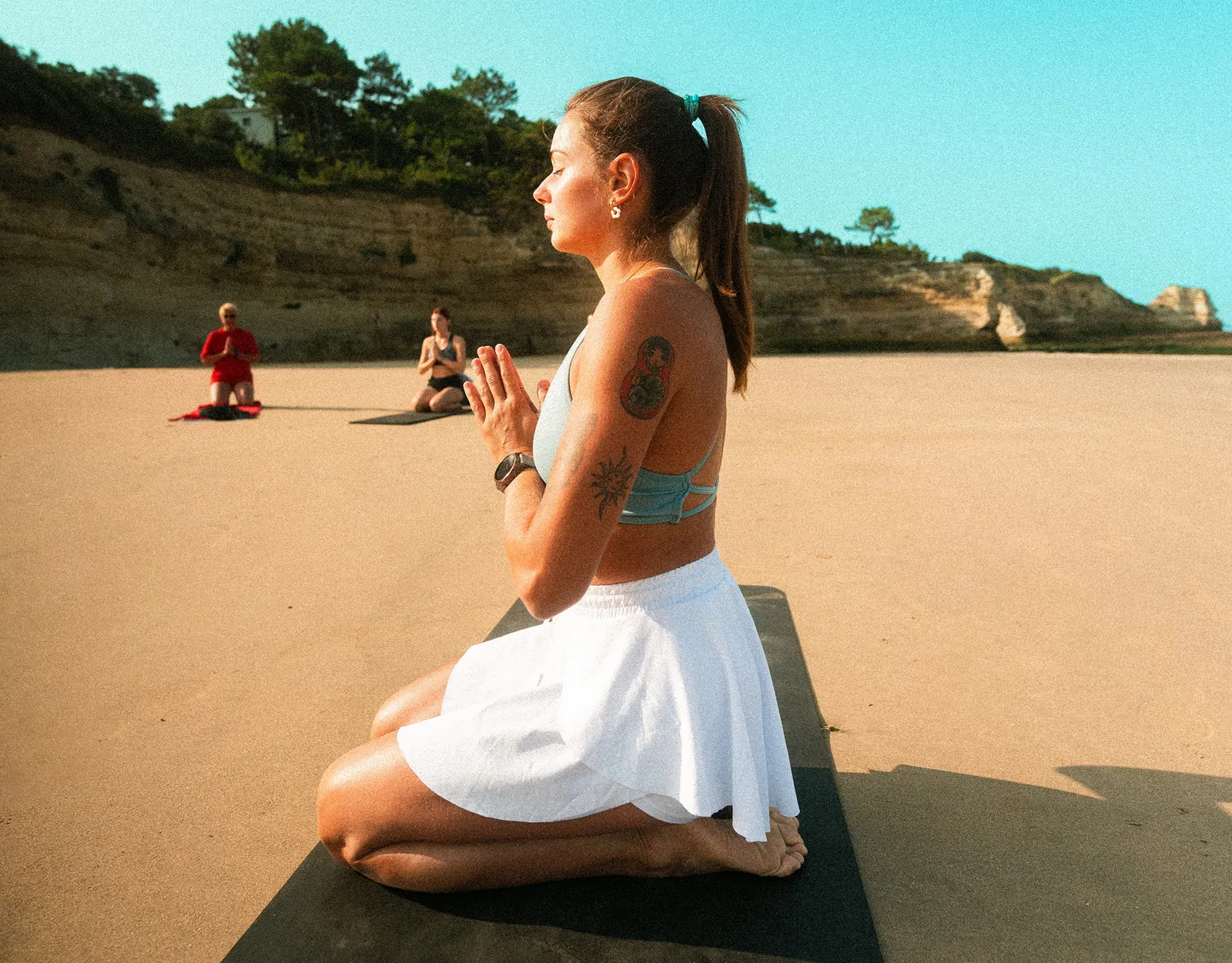 Femme en posture de méditation sur une plage, face à la falaise