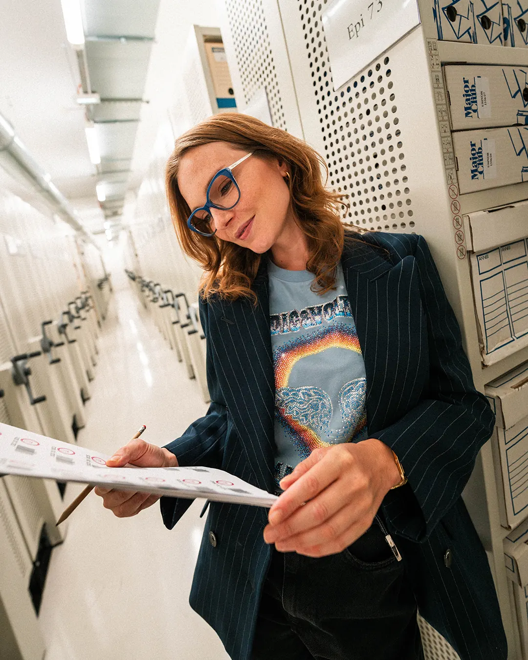 Femme à lunettes lisant un document dans une allée d’archives
