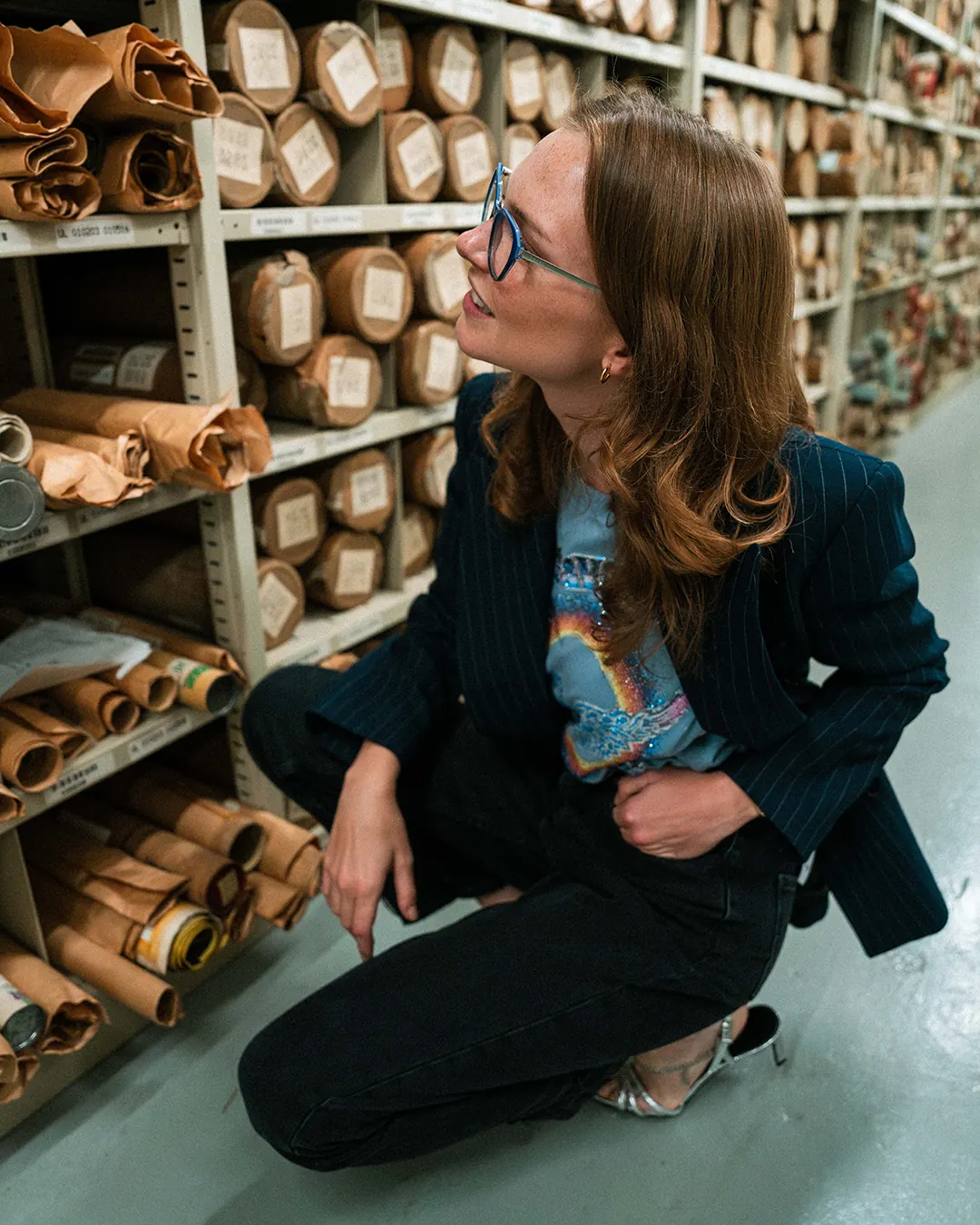 Femme accroupie entre des étagères de rouleaux d’archives
