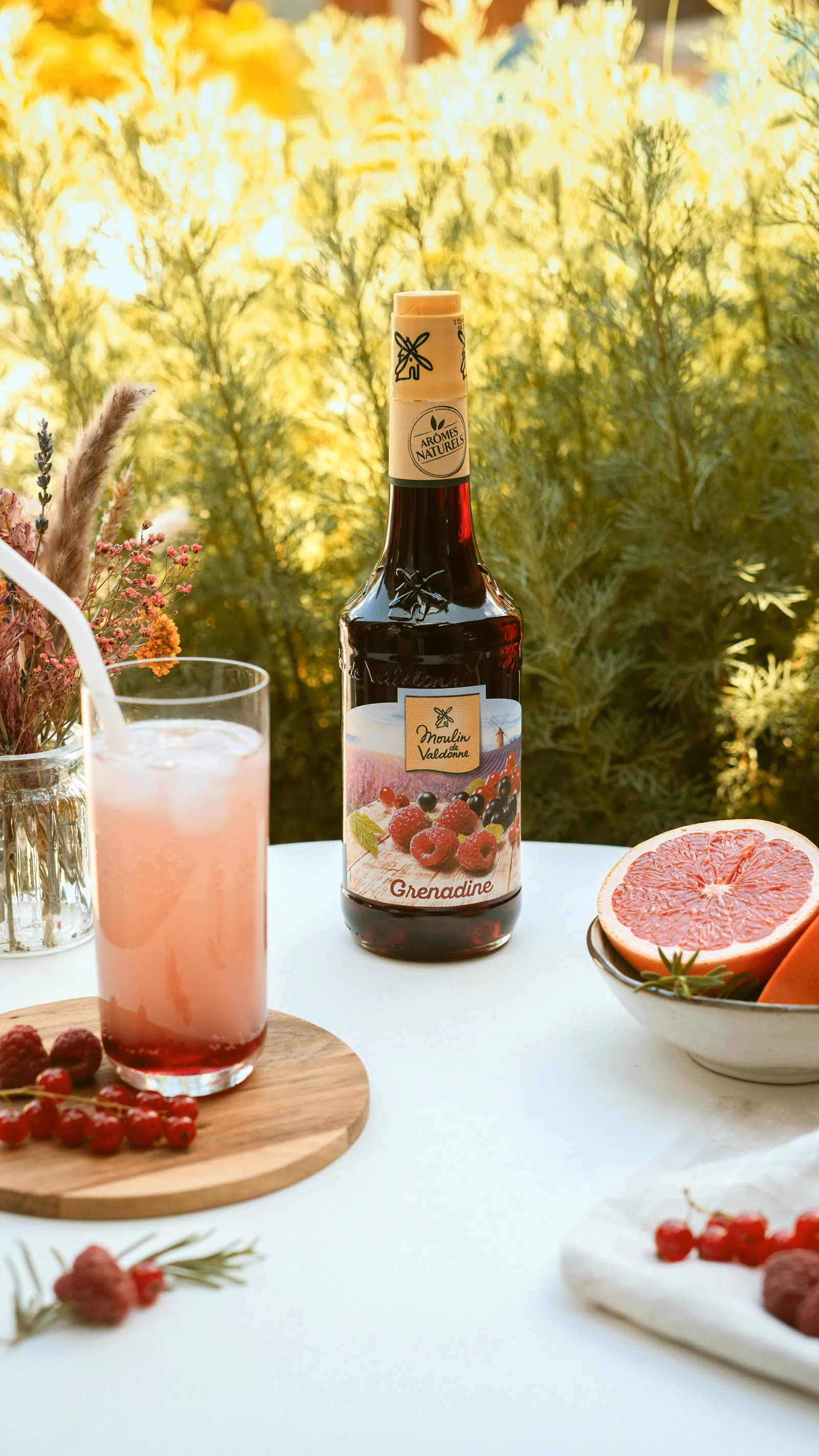 Verre de grenadine et bouteille Moulin de Valdonne sur une table au jardin